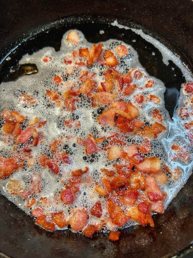 Crispy diced bacon in a cast iron pan with bacon fat.