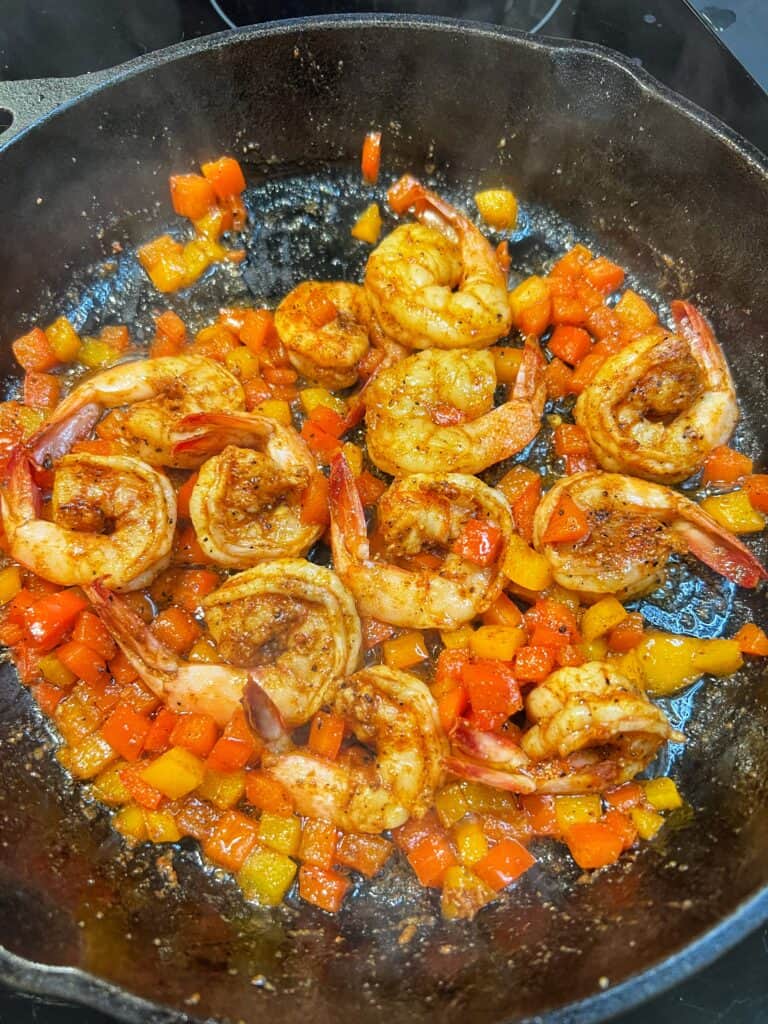 A cast iron pan of sautéed shrimp and diced bell peppers.