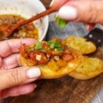 Me holding a piece of heirloom tomato bruschetta. The heirloom tomatoes are diced small and mixed with basil, red onion, garlic, olive oil and balsamic vinegar and placed on piece of crostini.