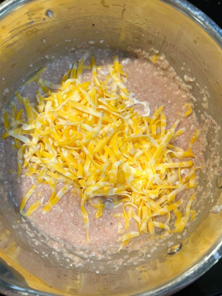 Shredded cheese into a pot of cooked grits.