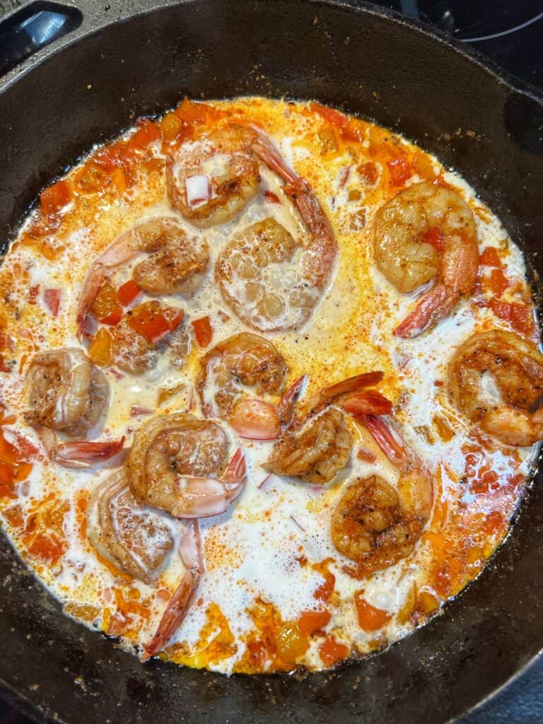Cream in a cast iron pan of sautéed shrimp and bell peppers. 
