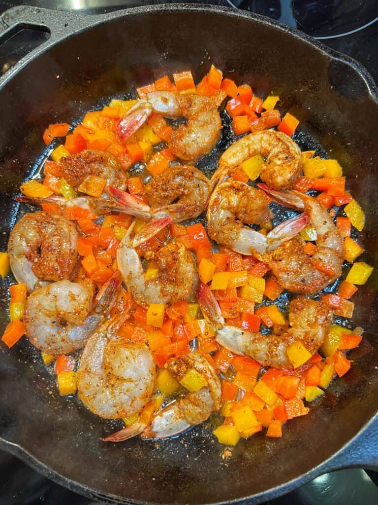 Sautéing shrimp and diced bell peppers in a cast iron pan for creamy cheesy shrimp and grits.