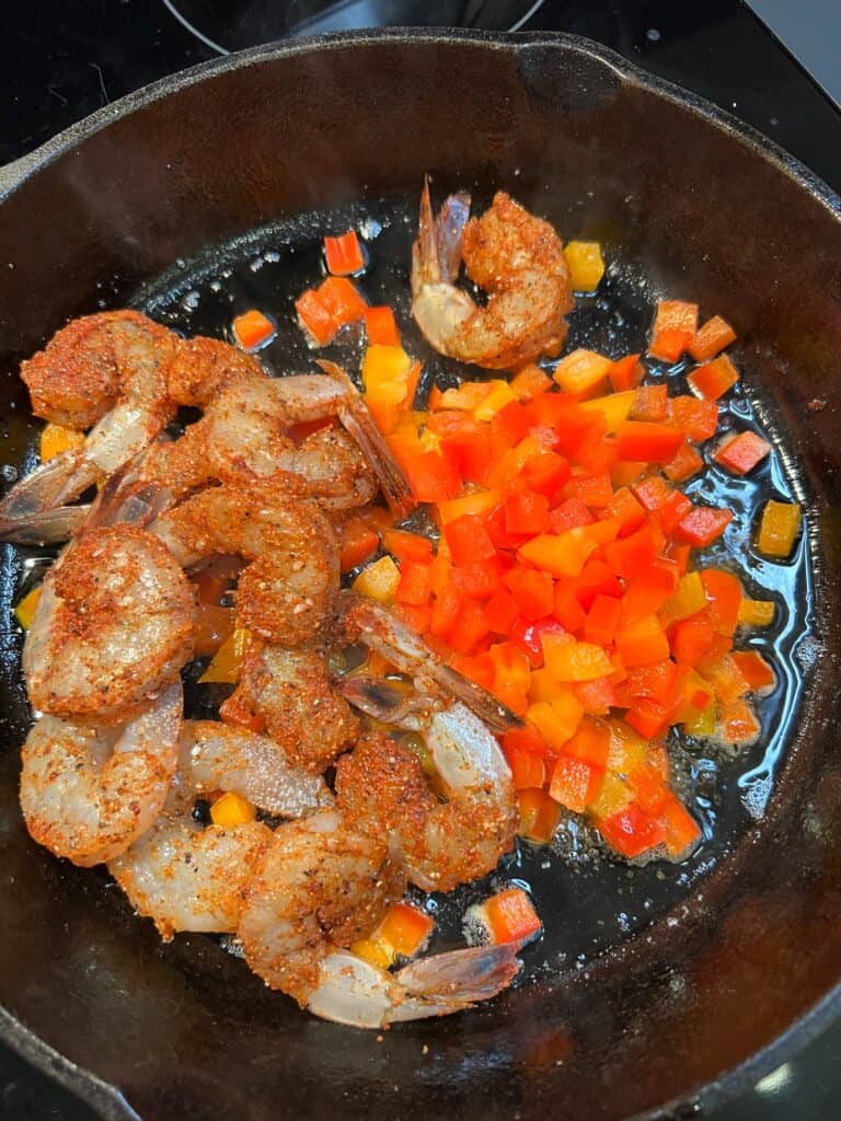 Seasoned shrimp and diced bell peppers in a cast iron pan.