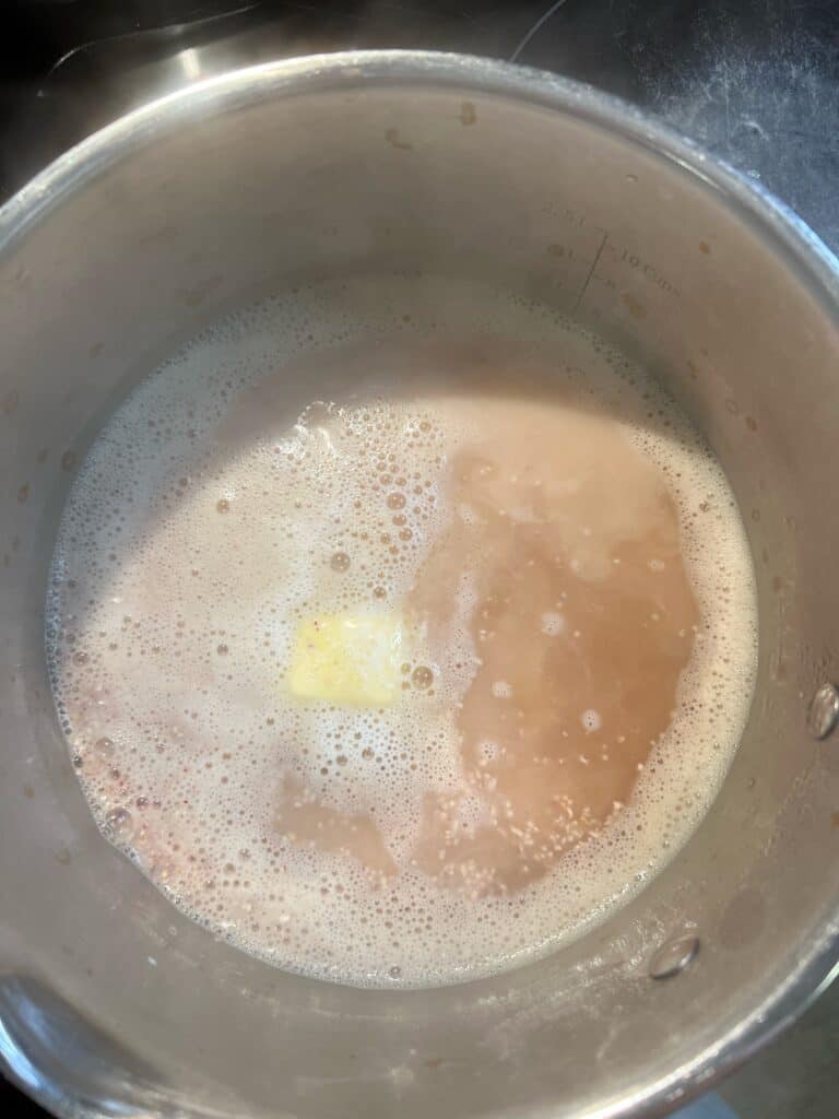 A stainless steel pot of stock, grits and butter for creamy cheesy shrimp and grits.