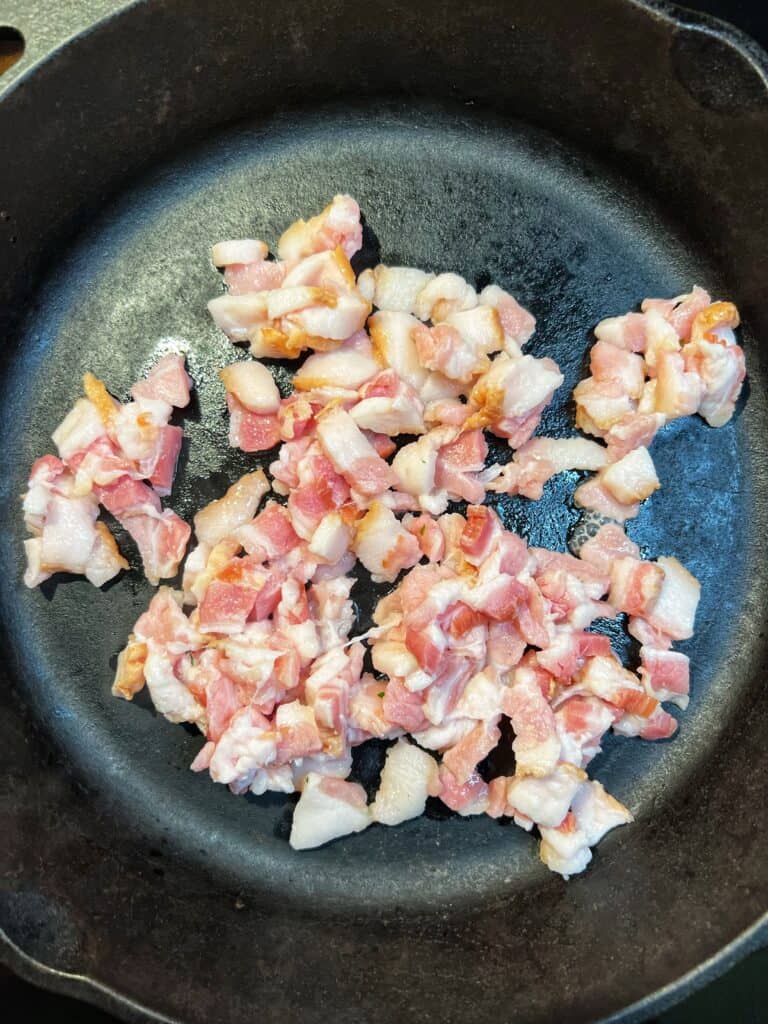 Diced bacon crisping in a cast iron pan.