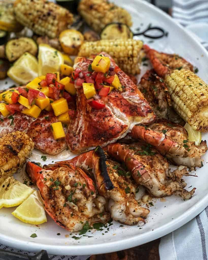 a plate of grilled grouper with mango salsa, shrimp, corn and vegetables