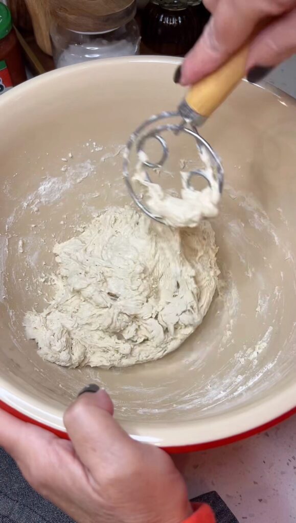 A rough ball of focaccia dough in a bowl. You can see part of the Danish dough whisk in the bowl.