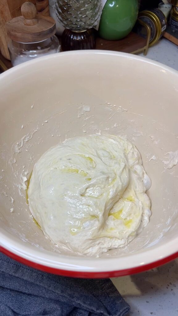 A ball of focaccia dough in a bowl covered in olive oil.