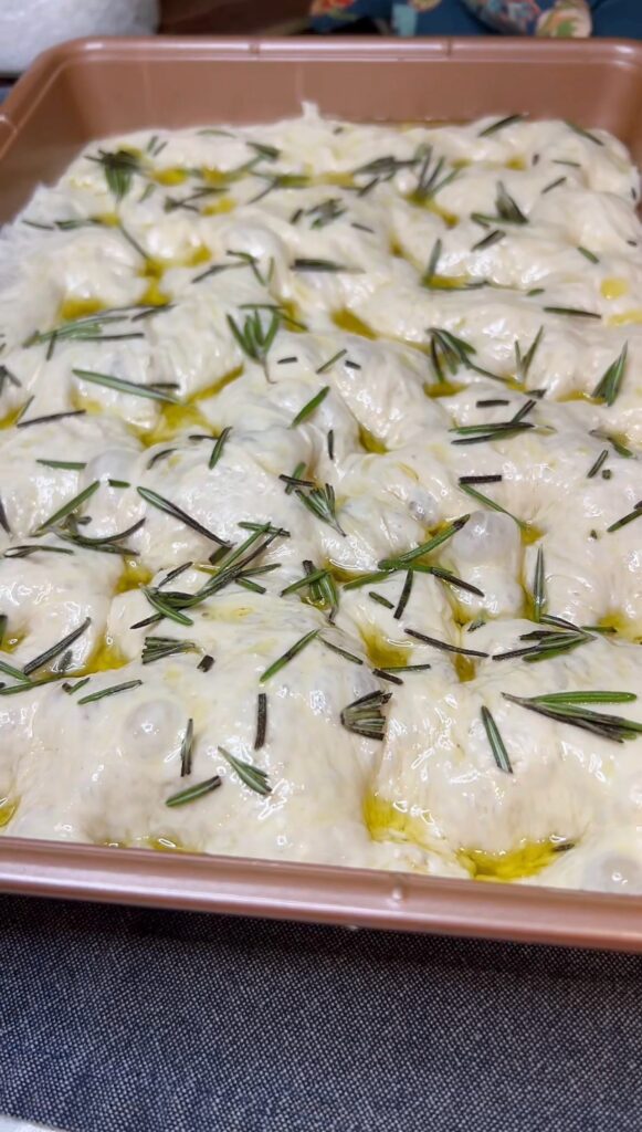 Fresh rosemary covering ready to bake focaccia dough in a pan.