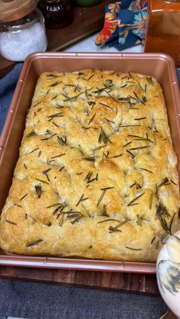 A pan of same day focaccia that has been baked with a topping of fresh rosemary.