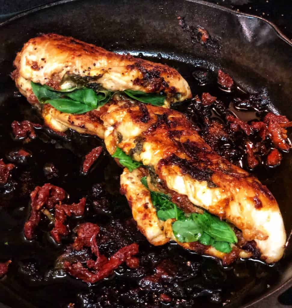 two pieces of spinach and sun dried tomato pesto chicken cooked in a cast iron pan