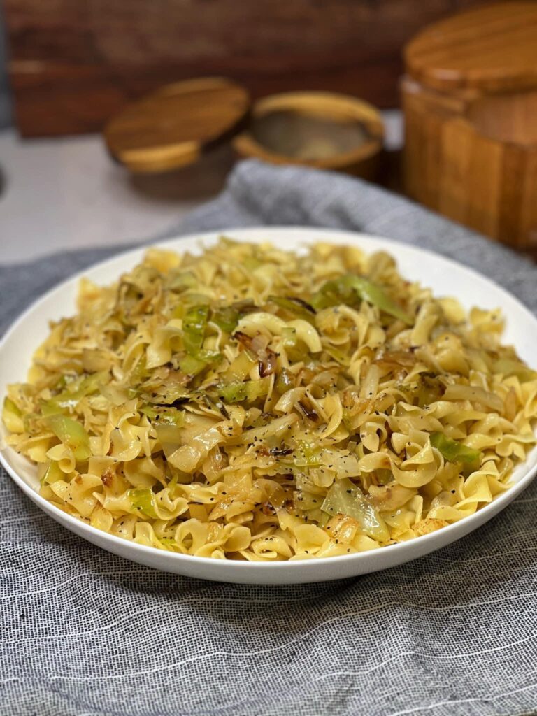 A white bowl filled with Haluski Cabbage and Noodles. The slightly browned, shredded cabbage is mixed with cooked egg noodles.