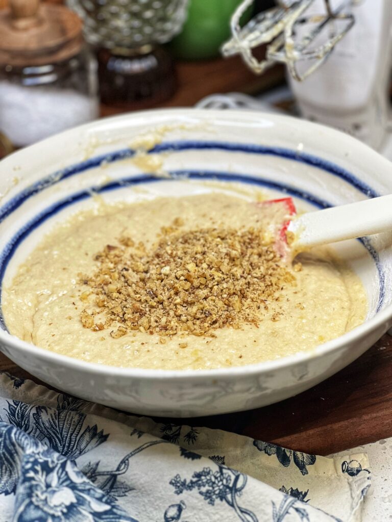 A white bowl trimmed inside with blue stripes holding banana nut bread butter. Chopped walnuts are sitting on the top.