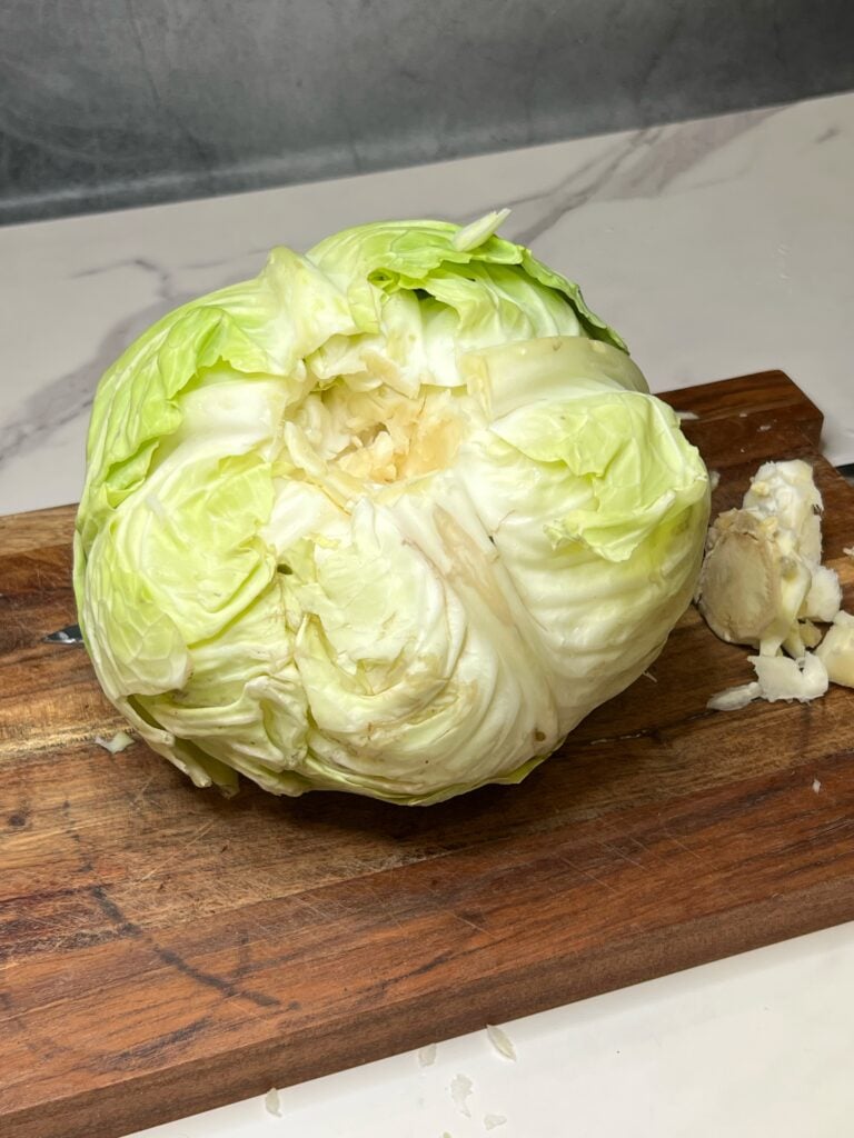 A head of green cabbage with the core removed sitting on a wooden cutting board.
