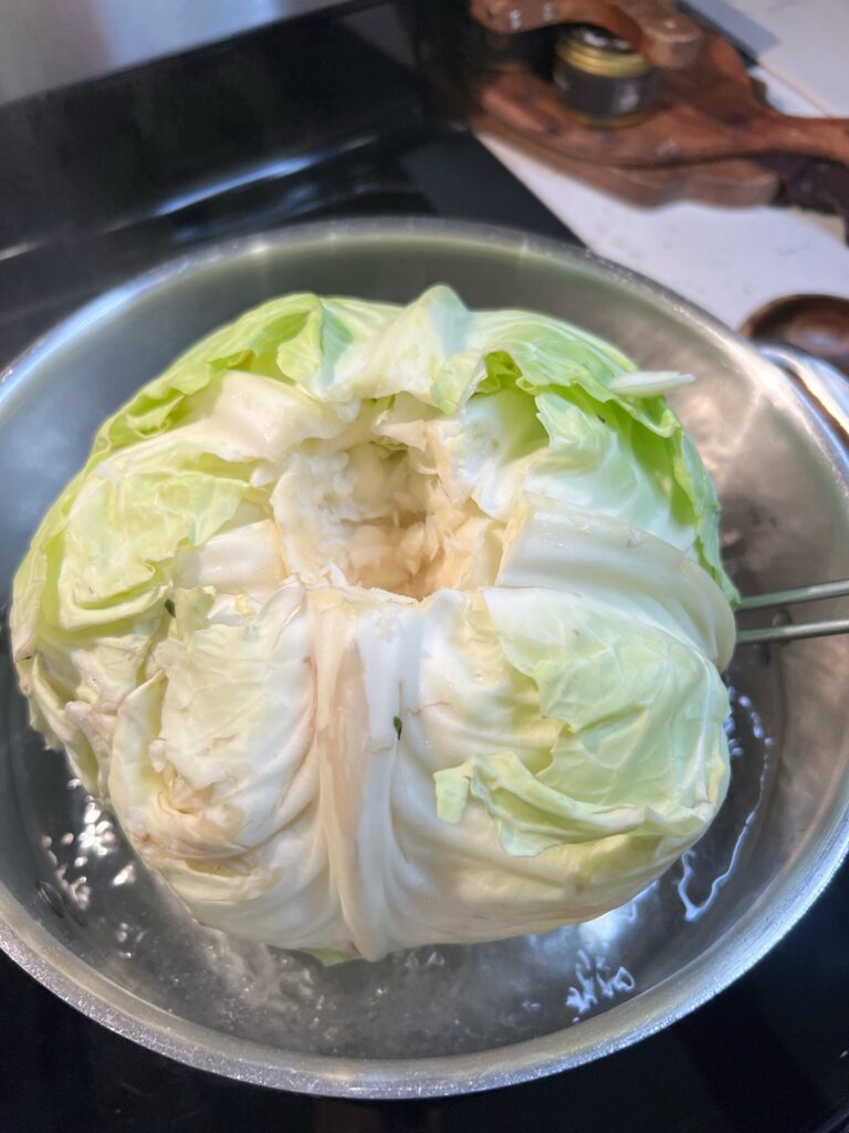 A head of green cabbage being lowered into a pot of simmering water.