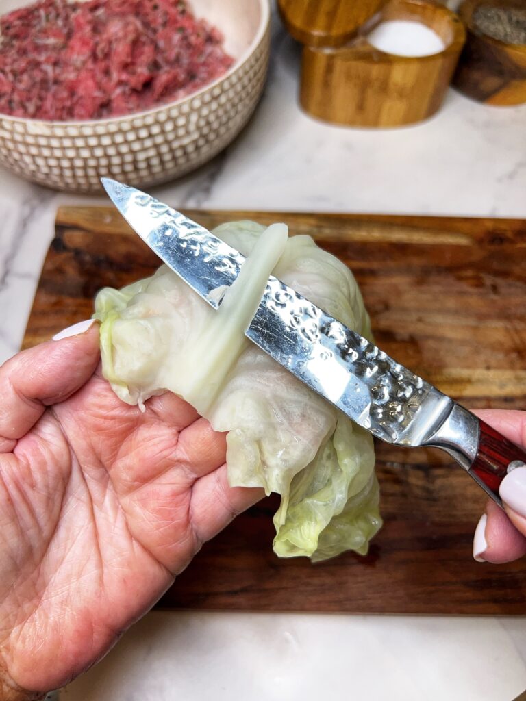 Trimming the core off of a steamed cabbage leaf with a paring knife.