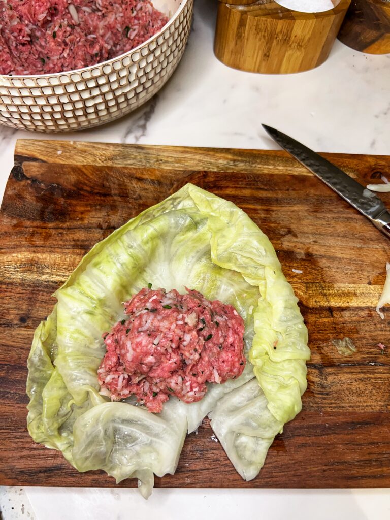 A steamed cabbage leaf laying on a wooden board filled with a ground meat mixture. 