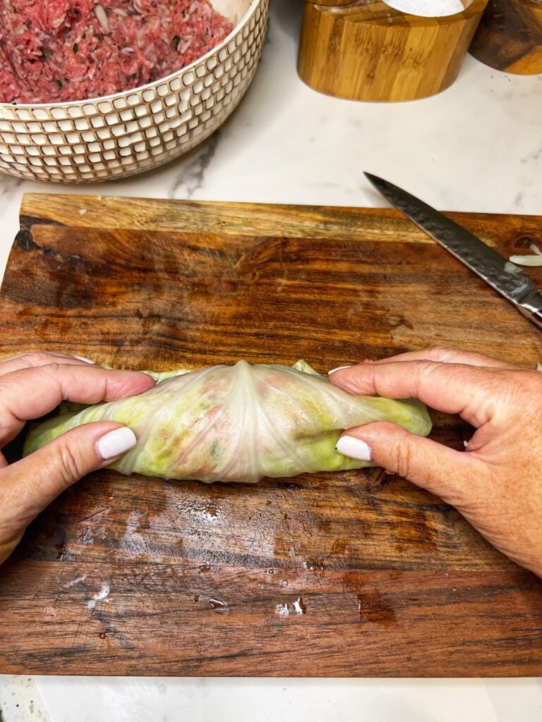 Rolling a cabbage leaf filled with a ground beef mixture on a wooden board.