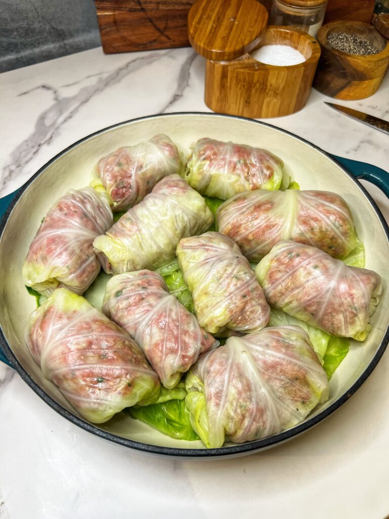 A shallow roasting pan filled with uncooked cabbage rolls. The pan is lined with cabbage leaves.