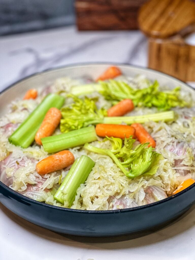 Cabbage rolls in a pan topped with sauerkraut, carrots and celery.