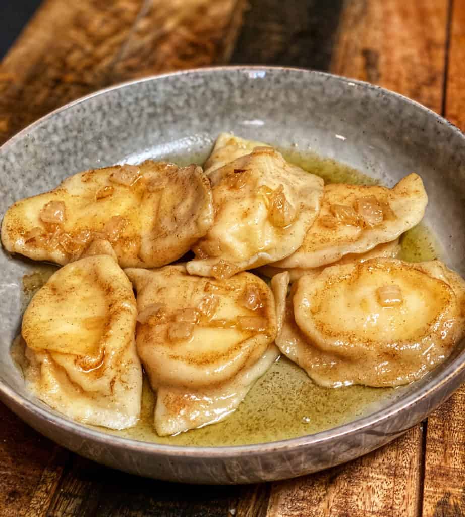 A grey plate of potato and cheese pierogies with butter and onions.