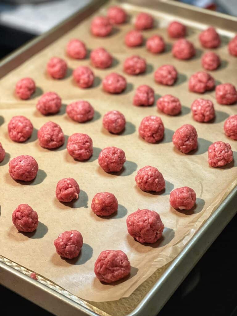 A parchment lined baking sheet filled with raw, mini meatballs for Spaghetti O's Pasta.