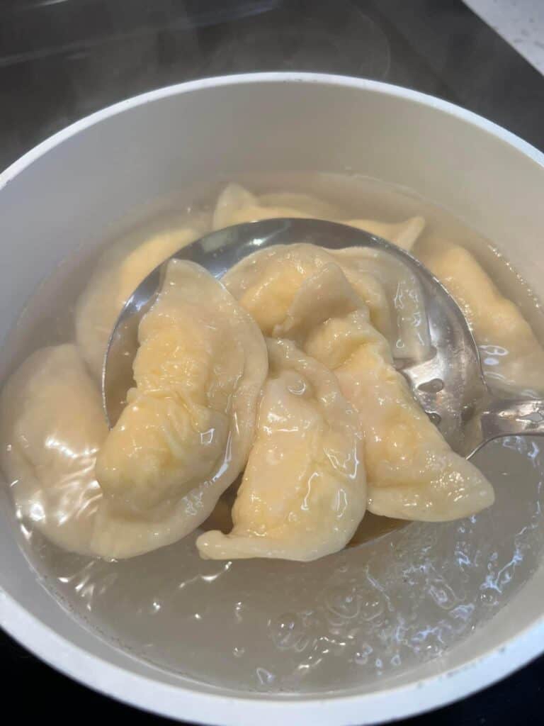 Boiled pierogies on a slotted spoon coming out of the water.