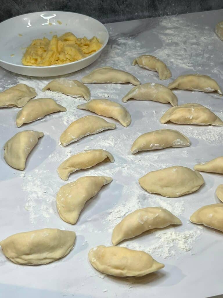 Filled pierogies sitting on a flat, floured surface.
