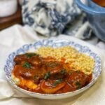 A bowl of steak with red gravy over mashed potatoes with a side of corn.
