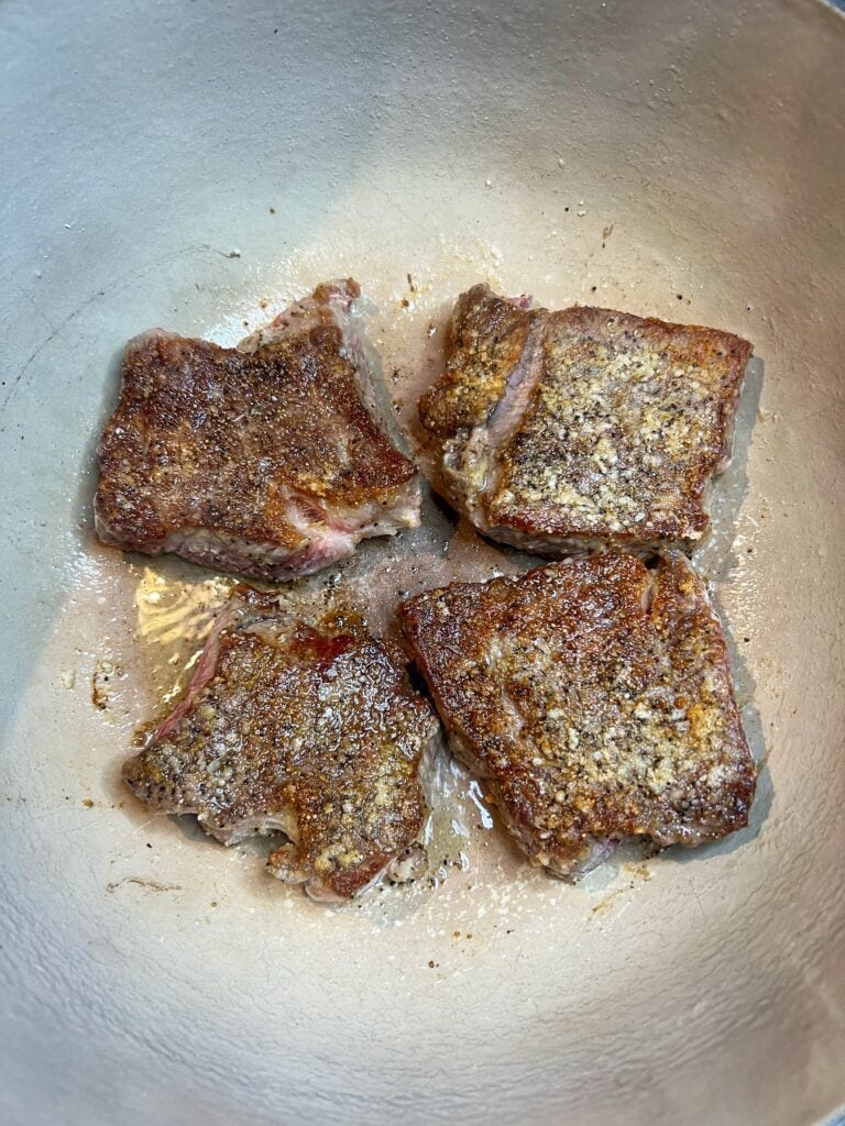 Four pieces of seared ribeye in a pot for Steak with Red Gravy.