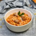 A white bowl of Spaghetti O's Pasta with Meatballs. The dish is garnished with fresh parsley and freshly grated Parmesan cheese.
