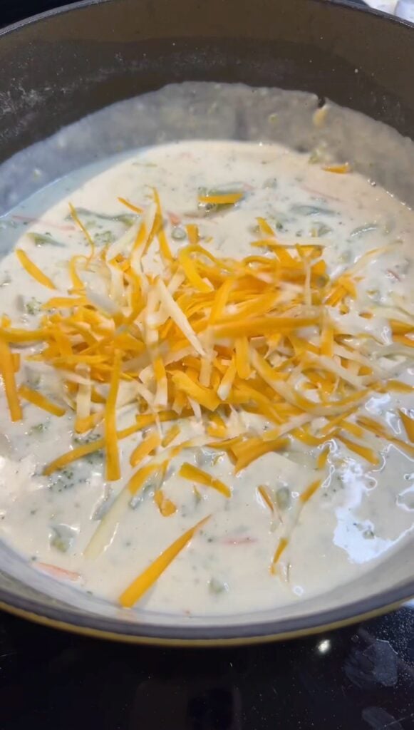 Shredded cheddar cheese being stirred into Broccoli Soup.