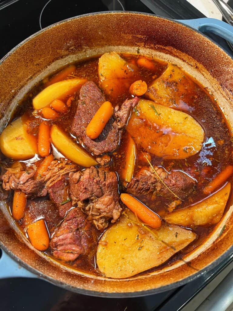 A Dutch oven filled with chunks of beef roast with halved potatoes and carrots.