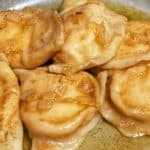 An up close shot of potato and cheese pierogies in a grey bowl covered in butter and onions.