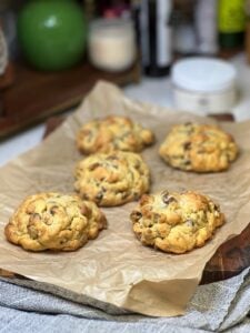 Five thick and fluffy, salted chocolate chip cookies sitting on brown parchment paper.