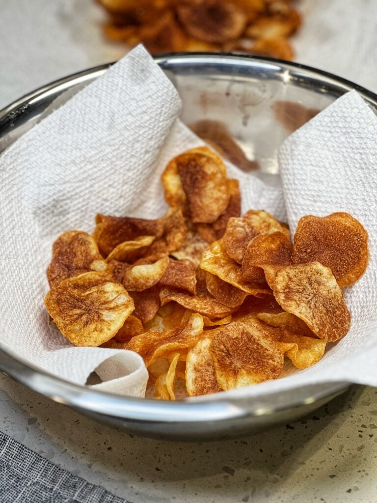 Crispy homemade potato chips in a stainless steel bowl lined with paper towels.
