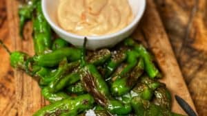 blistered shishito peppers on a wooden board with a side of Sriracha mayo