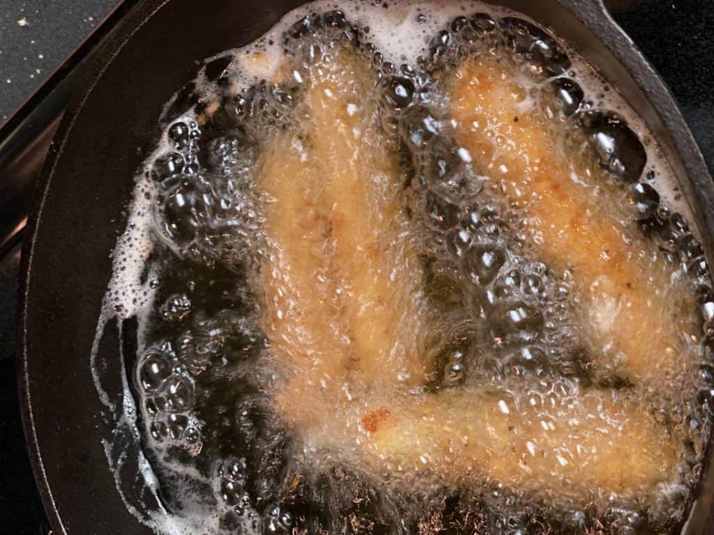 cheese sticks frying in a cast iron pan