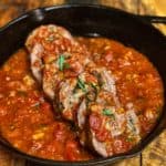 A large piece of braciole sliced with homemade tomato sauce in a cast iron pan.