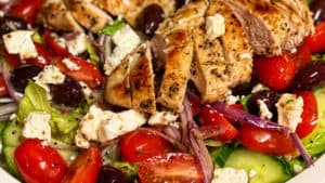 a white plate of Greek Salad with two chicken breasts sliced