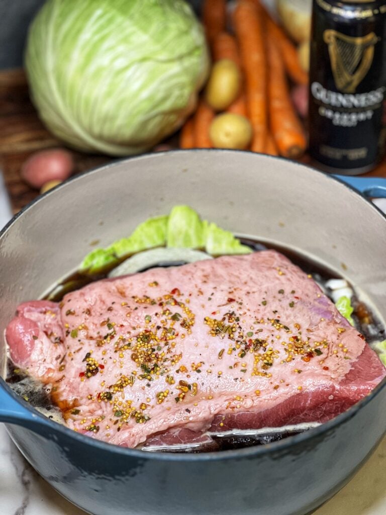 A seasoned piece of raw, brisket sitting in a pot with cabbage leaves, onions and beef stock.
