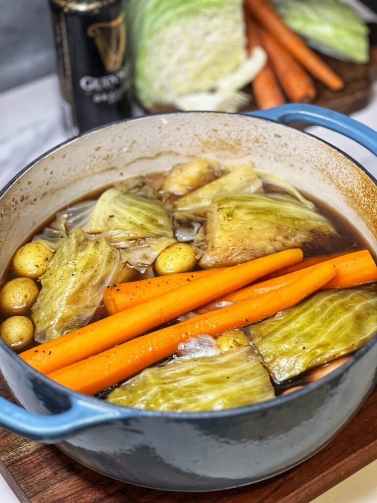 A Pot of cooked, Traditional Corned Beef and Cabbage. The pot contains corned beef, stock, cooked carrots, cabbage wedges and small potatoes.