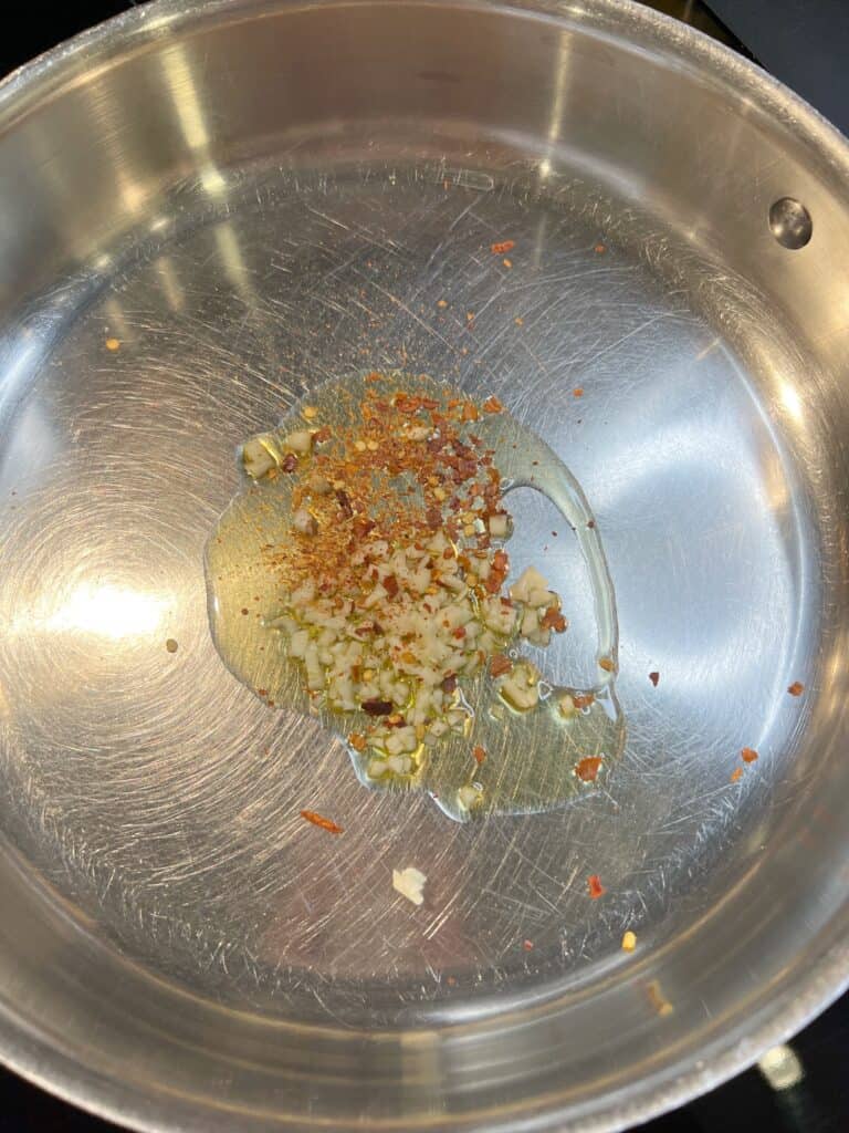 Minced garlic and crushed red pepper sautéing in olive oil in a stainless steel pan.