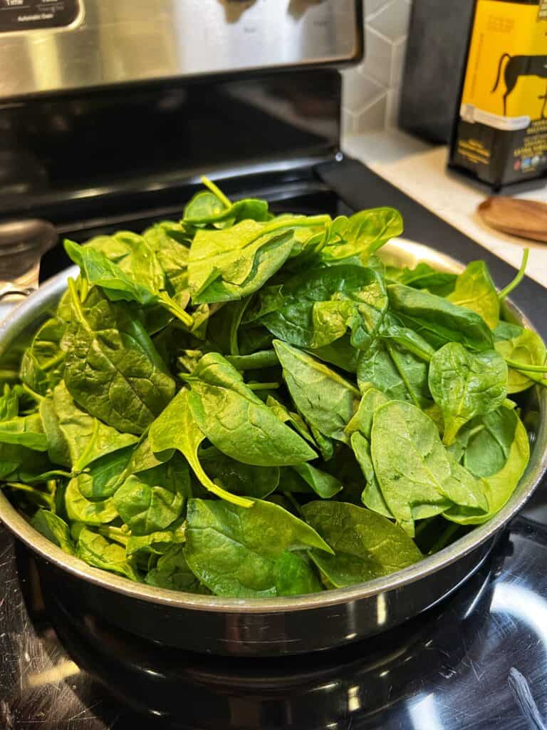Fresh baby spinach added to a stainless steel pan.