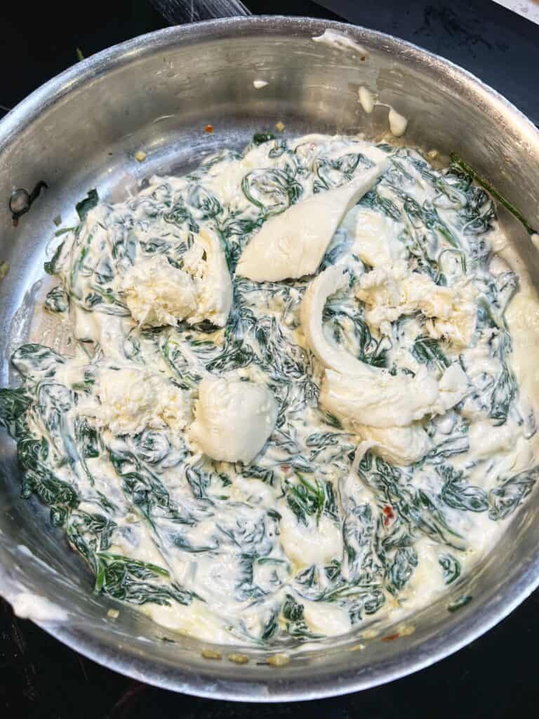 Pieces of fresh mozzarella added to a pan with wilted spinach and cream cheese.
