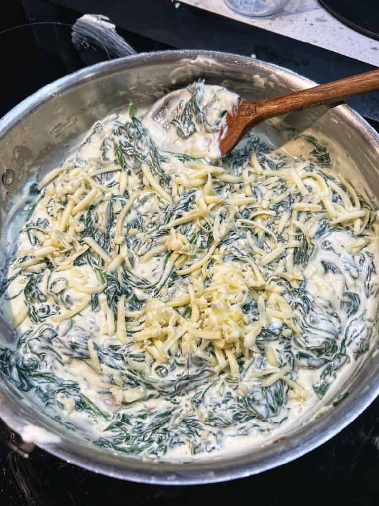 Shredded Gruyère added to a pan of wilted spinach and melted cream cheese.