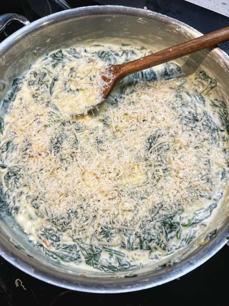 Freshly grated Parmesan cheese added to a pan of creamy spinach.