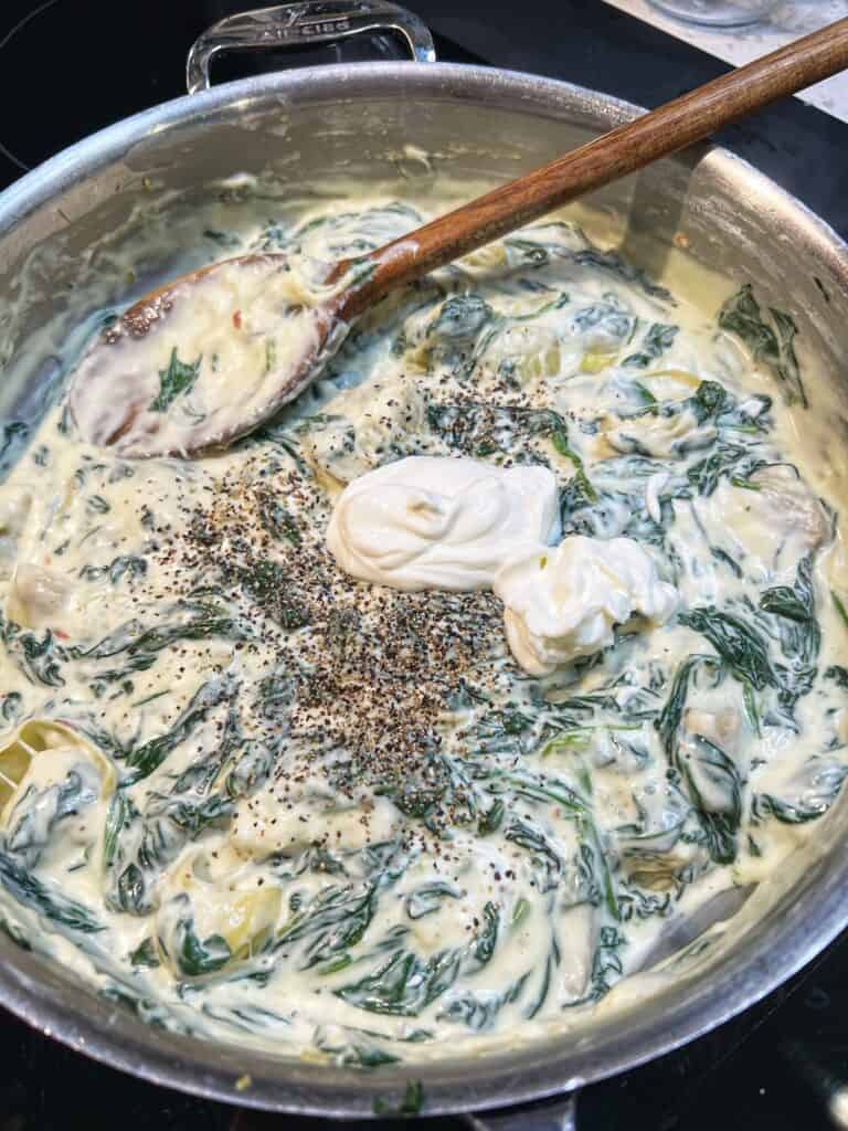 Sour cream and black pepper added to a pan with a creamy, cheesy spinach base and artichokes.