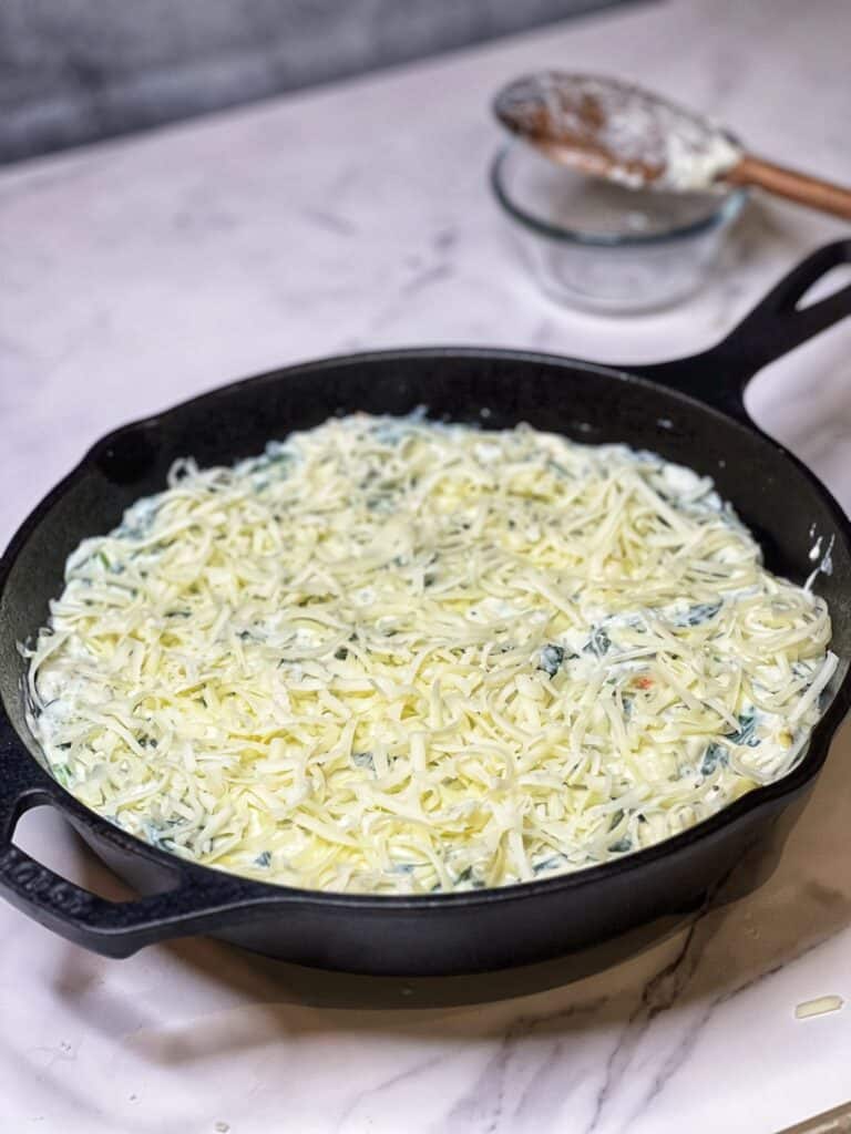 Shredded mozzarella covering a spinach artichoke dip that is in a cast iron pan.