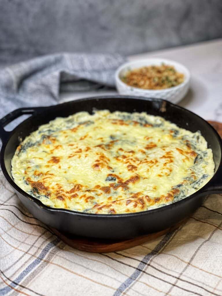A cast iron pan of baked six cheese spinach artichoke dip.